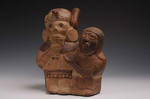Sculptural ceramic ceremonial vessel that represents an inhabitant of the underworld playing the pan flute and being embraced by a woman ML004336 - Moche style
